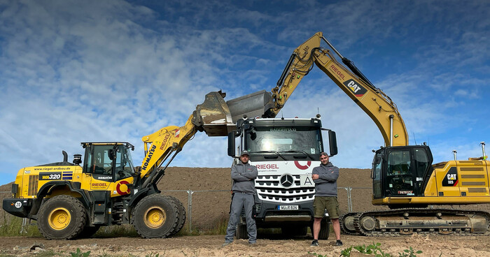 Zwei Bagger beladen gemeinsam einen Lkw, Mitarbeitende im Baustelleneinsatz.